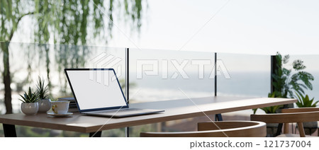 A close-up of a laptop with a white screen mockup on a table on a balcony with a stunning ocean view 121737004