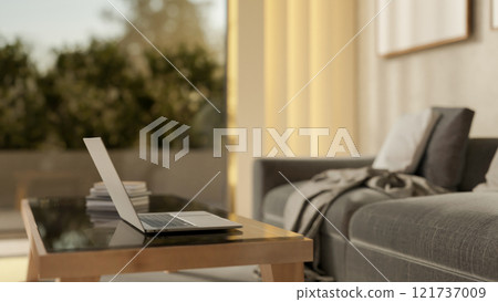 A close-up side view of a laptop on a coffee table in a modern and comfortable living room. A close-up side view of a laptop on a coffee table in a modern and comfortable living room. 121737009