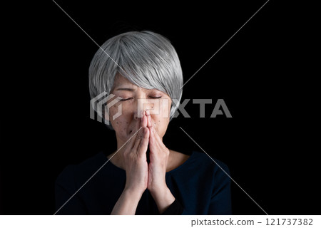 Senior woman with her eyes downcast and hands together 121737382