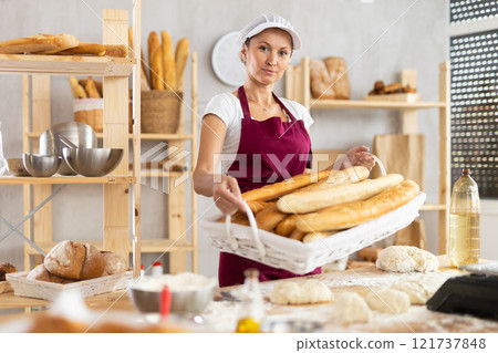 Young woman baker are standing near product range in bakery kitchen with basket loaf of baguettes 121737848