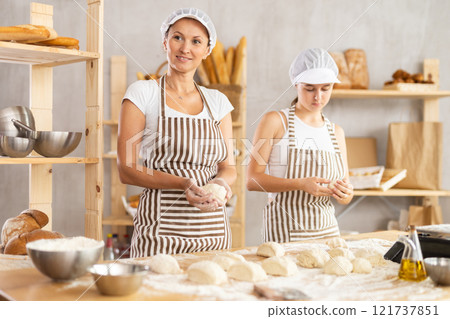 Female baker and her young assistant roll dough into balls to make delicious buns 121737851