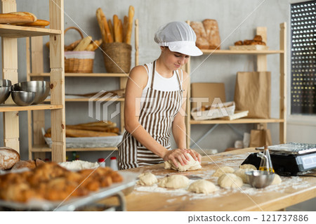 Teen girl works in bakery as baker, kneads dough, works with flour. 121737886