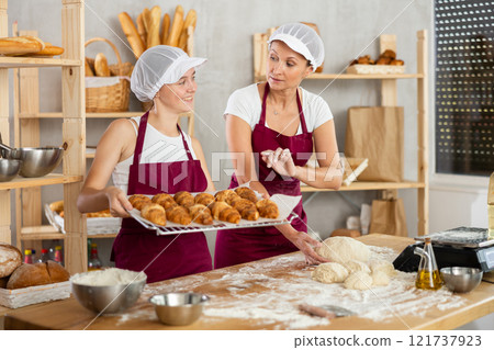 Adult female baker giving advice to young assistant in kitchen 121737923