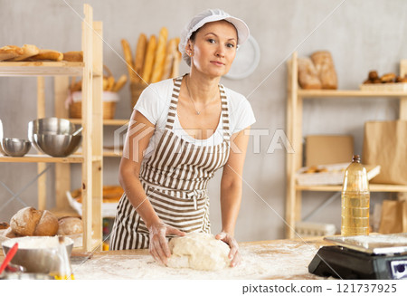 Woman works in bakery as baker, kneads dough, works with flour. 121737925