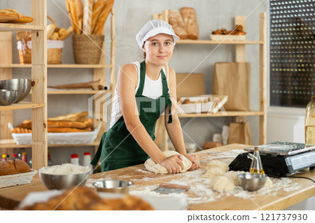 Teen girl works in bakery as baker, kneads dough, works with flour. Teen girl works in bakery as baker, kneads dough, works with flour. 121737930