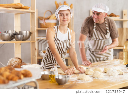 Teenage girl is kneading dough while male baker is controlling her 121737947