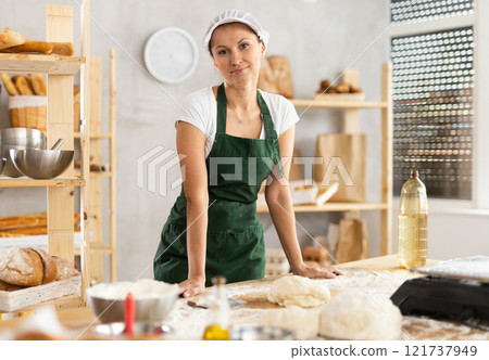 Woman works in bakery as baker, kneads dough, works with flour. 121737949