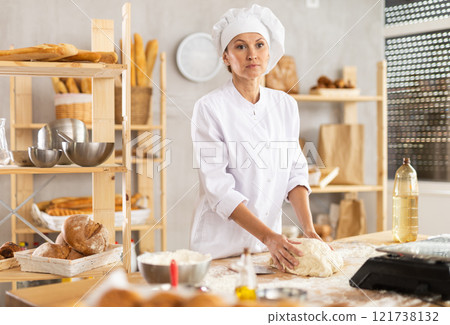 Working in bakery - woman kneads raw dough to make baguettes or croissants Working in bakery - woman kneads raw dough to make baguettes or croissants 121738132