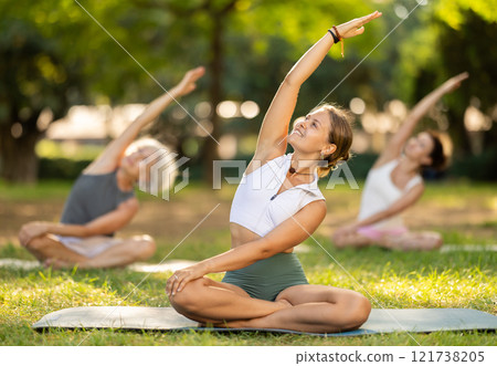 Girl stretching in lotus position group yoga session in park 121738205