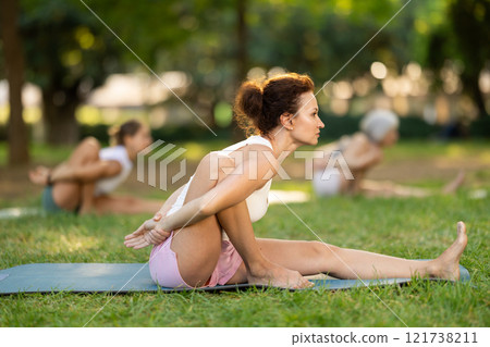 Fit woman performing Marichyasana at group yoga session in park 121738211