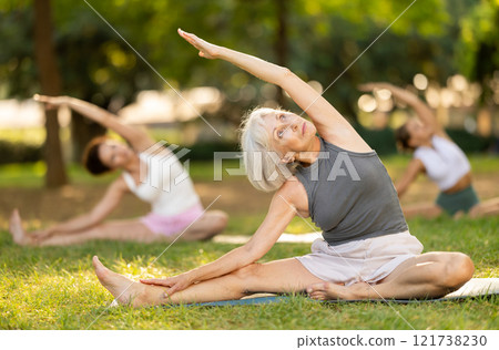 Elderly woman participating in outdoor yoga session in summer park 121738230