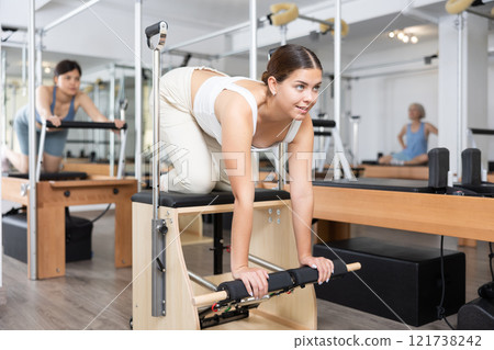 Mature woman practicing pilates stretching exercises on reformer at gym 121738242