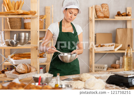 Middle-aged woman whipping ingredients in metal bowl 121738251