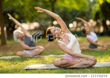 Woman stretching in lotus position during outdoor yoga class 121738254
