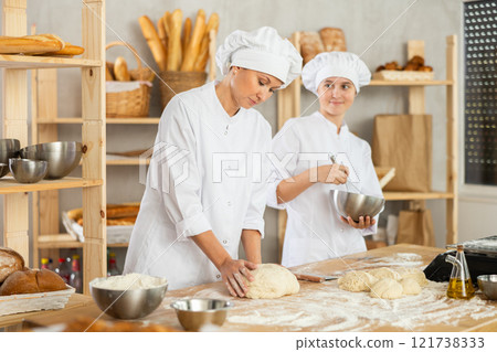 Experienced female cook teaches young girl how to make bread dough - they knead dough together and whisk eggs 121738333