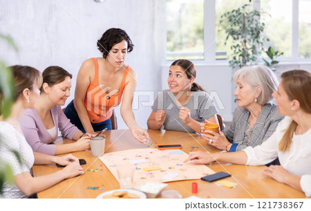 Women playing board game sitting at table in office 121738367
