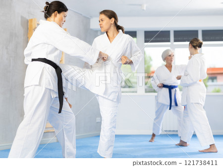 Karate lessons in the gym - women in pairs train punches and kicks in gym 121738411