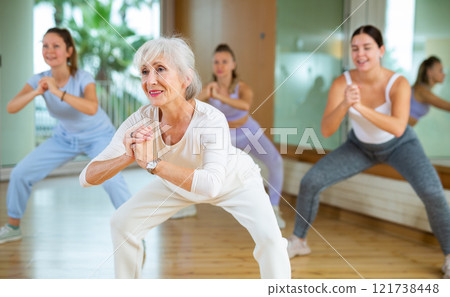Dynamic elderly woman practicing aerobic dance in training hall 121738448