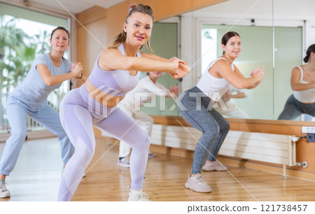 Smiling active women of different ages making squats during dancing training with coach in fitness studio 121738457
