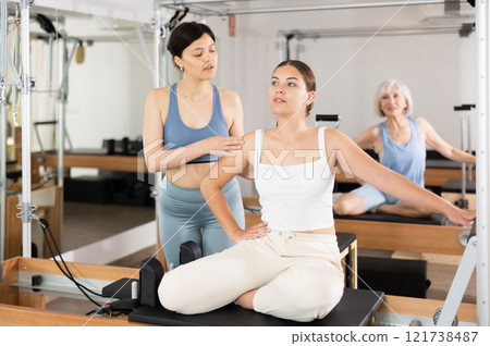 Woman doing pilates in fitness studio with female personal trainer controlling movements Woman doing pilates in fitness studio with female personal trainer controlling movements 121738487