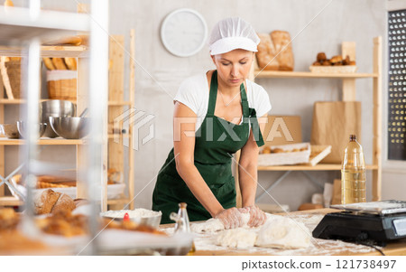 Middle-aged woman baker rolls out dough in bakery 121738497