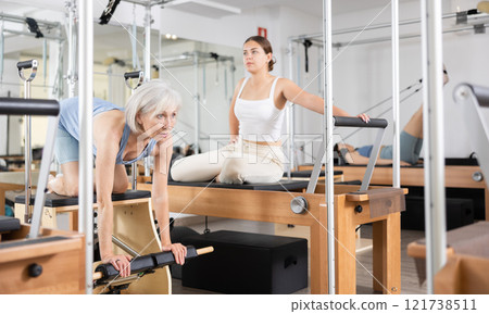 Sporty elderly woman practicing pilates exercises on combo chair 121738511