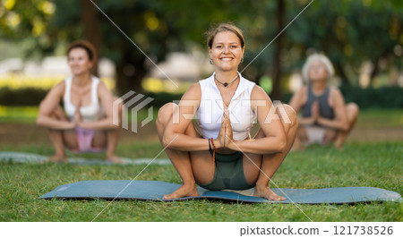 Girl performing Garland Pose during group yoga in park 121738526