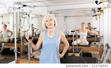 Smiling elderly woman leaning on wunda chair in pilates studio Smiling elderly woman leaning on wunda chair in pilates studio 121738547