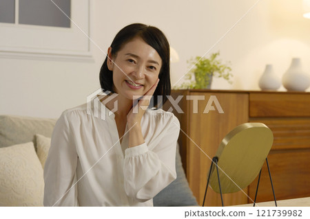 一位 50 多歲的女性晚上在客廳做皮膚護理，看著鏡頭 121739982