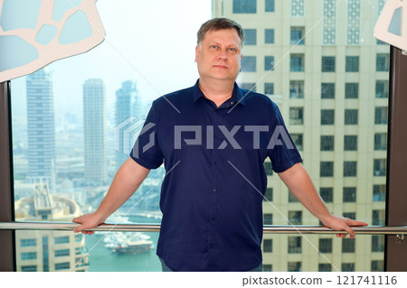 A blond man in a blue shirt against the backdrop of big city buildings 121741116