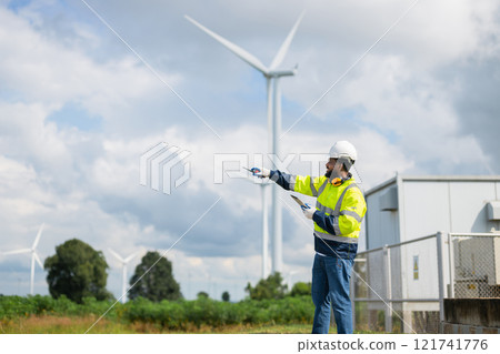 man in a yellow and black safety vest points at a wind turbine 121741776