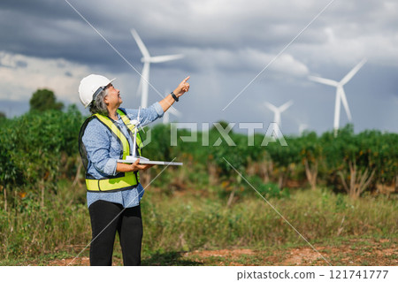 woman wearing a safety vest and a hard hat points to a wind turbine woman wearing a safety vest and a hard hat points to a wind turbine 121741777