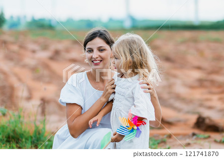 woman and a little girl are standing in a field. The woman is holding a colorful kite 121741870