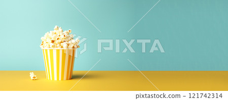a bowl of yellow popcorn with scattered kernels on a blue background. The playful scene evokes fun and excitement, ideal for cinema or film-related themes 121742314