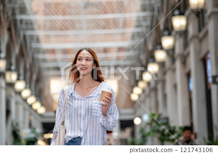 Woman is walking down a hallway with a cup of coffee in her hand Woman is walking down a hallway with a cup of coffee in her hand 121743106