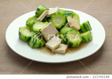 close up view of stir fried luffa with hard tofu in a ceramic dish on wooden table. asian homemade style healthy food concept. close up view of stir fried luffa with hard tofu in a ceramic dish on wooden table. asian homemade style healthy food concept. 121743149