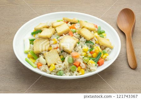 close up view of fried rice with hard tofu and vegetable in a ceramic dish on wooden table. vegan homemade style food concept. close up view of fried rice with hard tofu and vegetable in a ceramic dish on wooden table. vegan homemade style food concept. 121743367