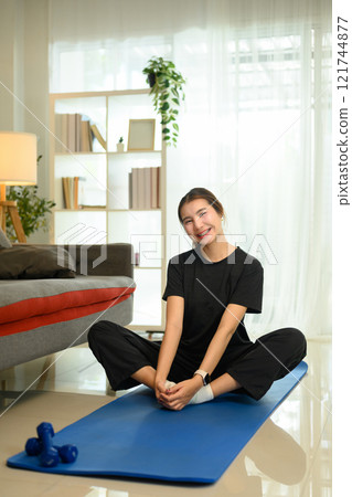 Young asian woman sitting in butterfly pose, stretching muscles on mat during home workout 121744877