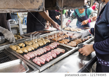 Close-up of the vendors grilling Taiwanese sausage and sticky rice (glutinous rice) sausage in the night market in Taiwan. This is one of the street snacks popular among tourists in Taiwan. Close-up of the vendors grilling Taiwanese sausage and sticky rice (glutinous rice) sausage in the night market in Taiwan. This is one of the street snacks popular among tourists in Taiwan. 121744945