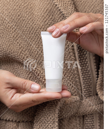 Closeup of woman in brown bathrobe holding squeeze cream tube in hands, cosmetic mockup 121745387