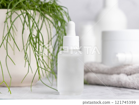 White glass dropper bottle on marble near green plant close up, cosmetic mockup White glass dropper bottle on marble near green plant close up, cosmetic mockup 121745399