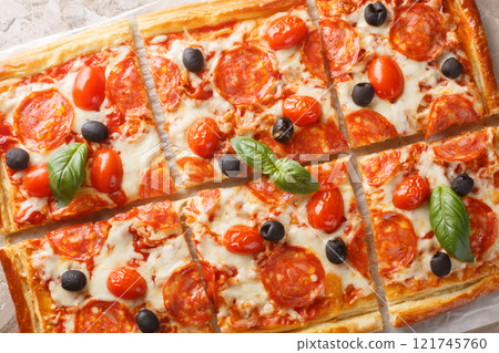 Tasty baked Puff pastry tart pizza style with pepperoni sausage, olives, tomatoes and mozzarella cheese close-up on parchment. Horizontal top view Tasty baked Puff pastry tart pizza style with pepperoni sausage, olives, tomatoes and mozzarella cheese close-up on parchment. Horizontal top view 121745760