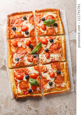 Hot puff pastry pizza pie with salami, olives, mozzarella cheese and tomato sauce close-up on parchment paper. Vertical top view Hot puff pastry pizza pie with salami, olives, mozzarella cheese and tomato sauce close-up on parchment paper. Vertical top view 121745761