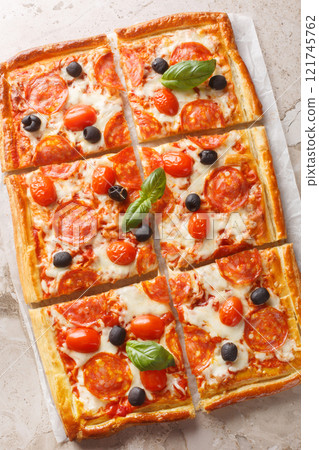 Homemade puff pastry pie with sausage, olives, tomatoes and mozzarella cheese like pizza pepperoni close-up on parchment. Vertical top view 121745762