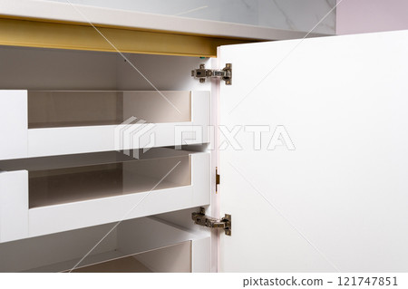 A modern, empty kitchen cabinet featuring sleek white design and transparent storage spaces. 121747851