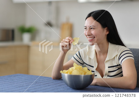 Happy asian woman holding potato chips looking away 121748378