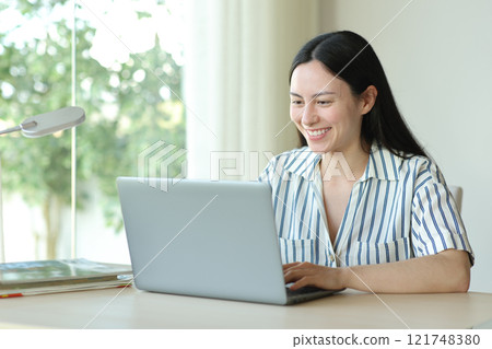 Happy asian woman using laptop in a room Happy asian woman using laptop in a room 121748380