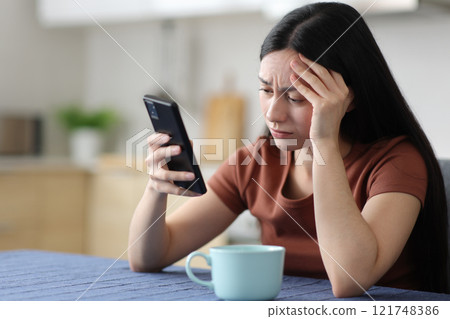 Worried asian woman checking smart phone in the kitchen 121748386