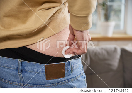 Cropped photo of man uses cotton pad to clean or press injection site on his lower back after administering shot. 121748462