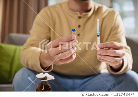 Close of male model holding jar with medicine and clean, disinfected syringe preparing medical tools for injecting treatment at home. 121748474